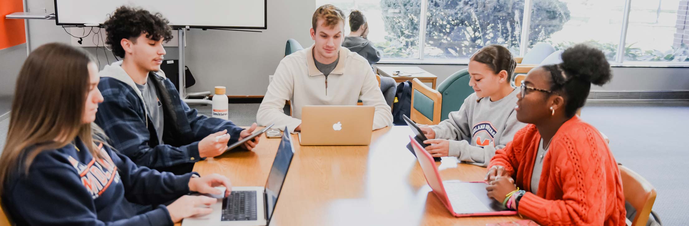 Students sitting around a table with laptops at library